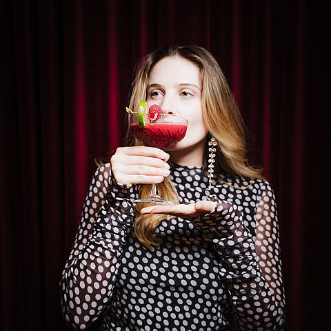 Woman in polka dot dress holding a red cocktail with lime and raspberry garnish