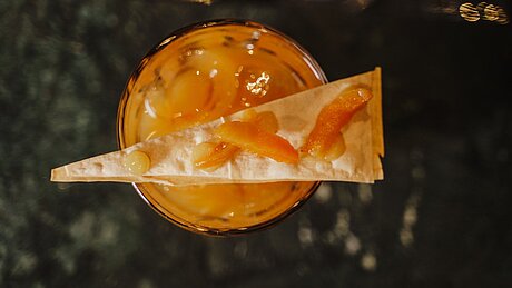 Orangener Cocktail mit Eis, garniert mit Dreieck-Cracker und kandierter Orangenschale