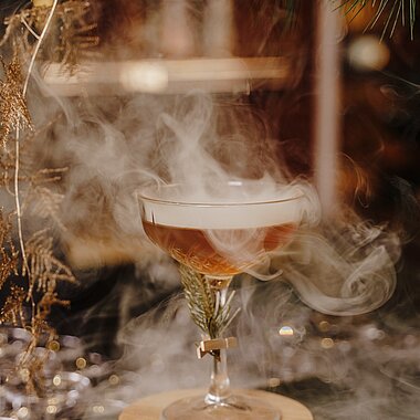 Rauchiger Cocktail in einem Kristallglas mit Rosmaringarnitur auf Holzuntersetzer